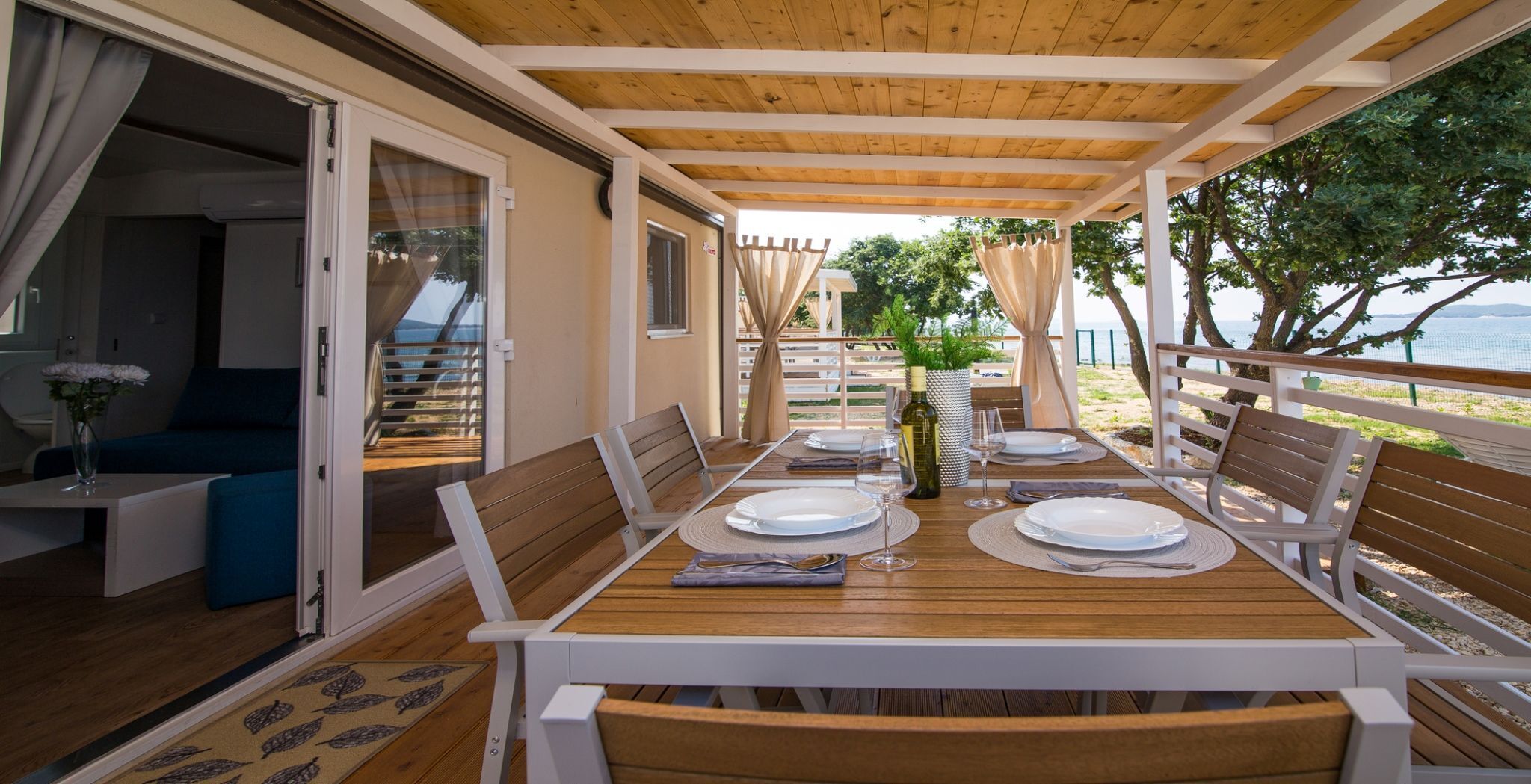 Un'area pranzo con un tavolo in legno apparecchiato per quattro persone, sedie bianche e vista sul mare.