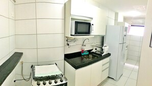 Eine kleine Küche mit weißen Schränken, einer schwarzen Arbeitsplatte, einer Mikrowelle, einem Spülbecken mit Armatur, einem kleinen Herd und einem Kühlschrank.