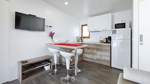 A compact kitchen with a TV, a microwave, and a refrigerator. There is a small dining area with two white chairs and a table.