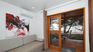 A modern living room with a grey sofa, a large abstract painting, and a sliding glass door leading to an outdoor deck with a table and chairs.