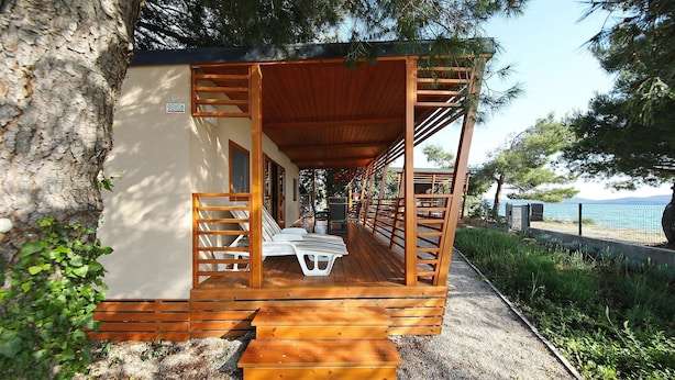 A wooden deck with a covered seating area, a gravel path, and a view of the sea.