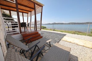 Un espacio de estar techado al aire libre con sillas de mimbre y una mesa de madera, con vistas a un cuerpo de agua y colinas.