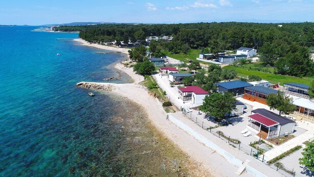 A coastal area with a beach, clear blue water, and several buildings with red roofs. - Mobile Home Plumeria 1 (Biograd)