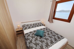 Una camera da letto piccola e ordinata, con un letto, lampade sui comodini, una finestra vista mare e pavimento in legno.