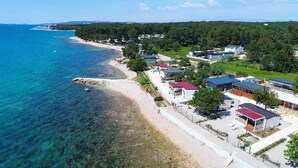 A coastal area with a beach, clear blue water, and several buildings with red roofs. - Mobile Home Plumeria 3 (Biograd)