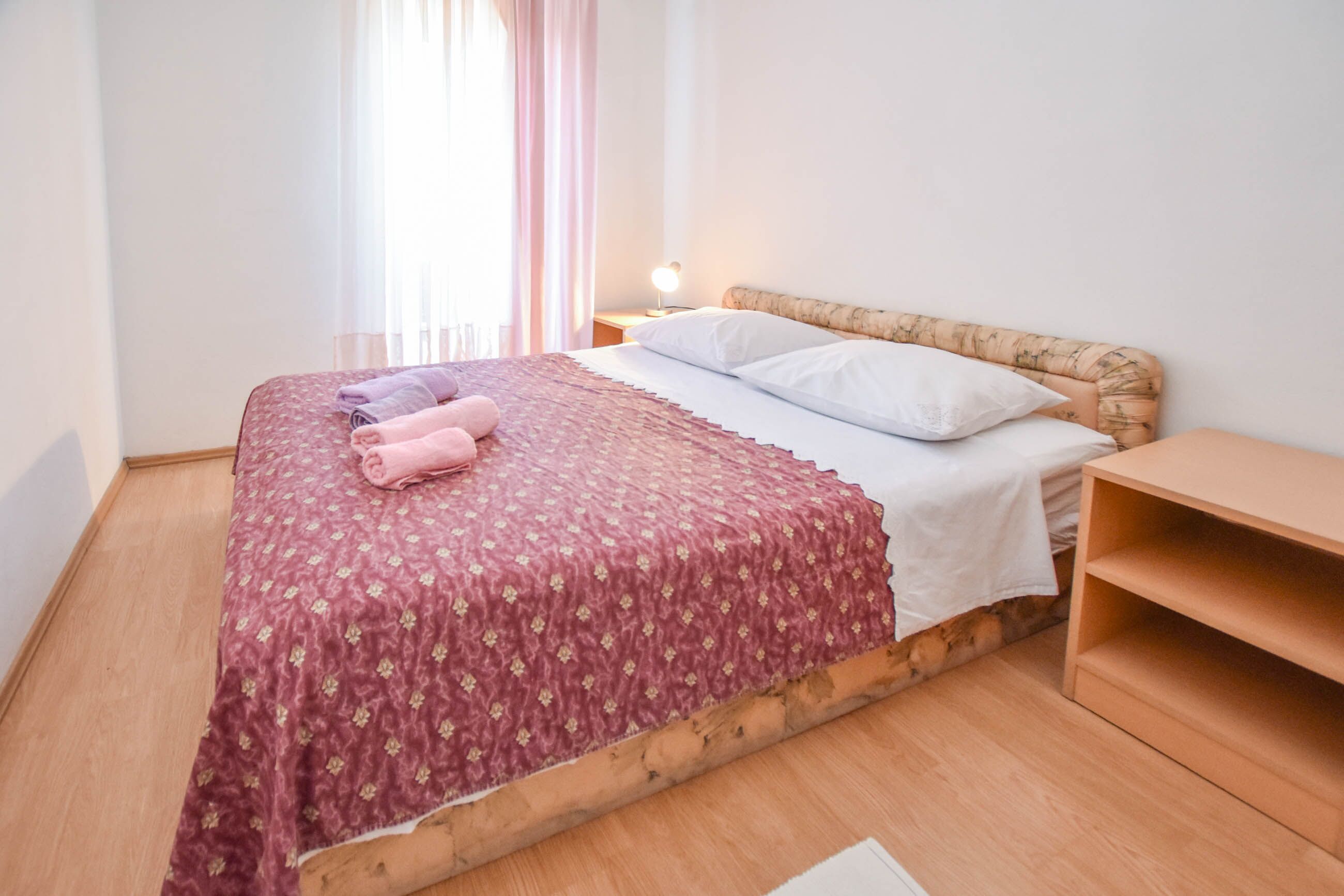 A neatly made bed with a floral-patterned bedspread and pillows, a bedside lamp, and a wooden nightstand.