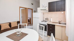 A compact kitchen with a stove, sink, and white cabinets. There is a dining table with chairs and a small glass table with decorative items. - Apartments Grapevines (Biograd)
