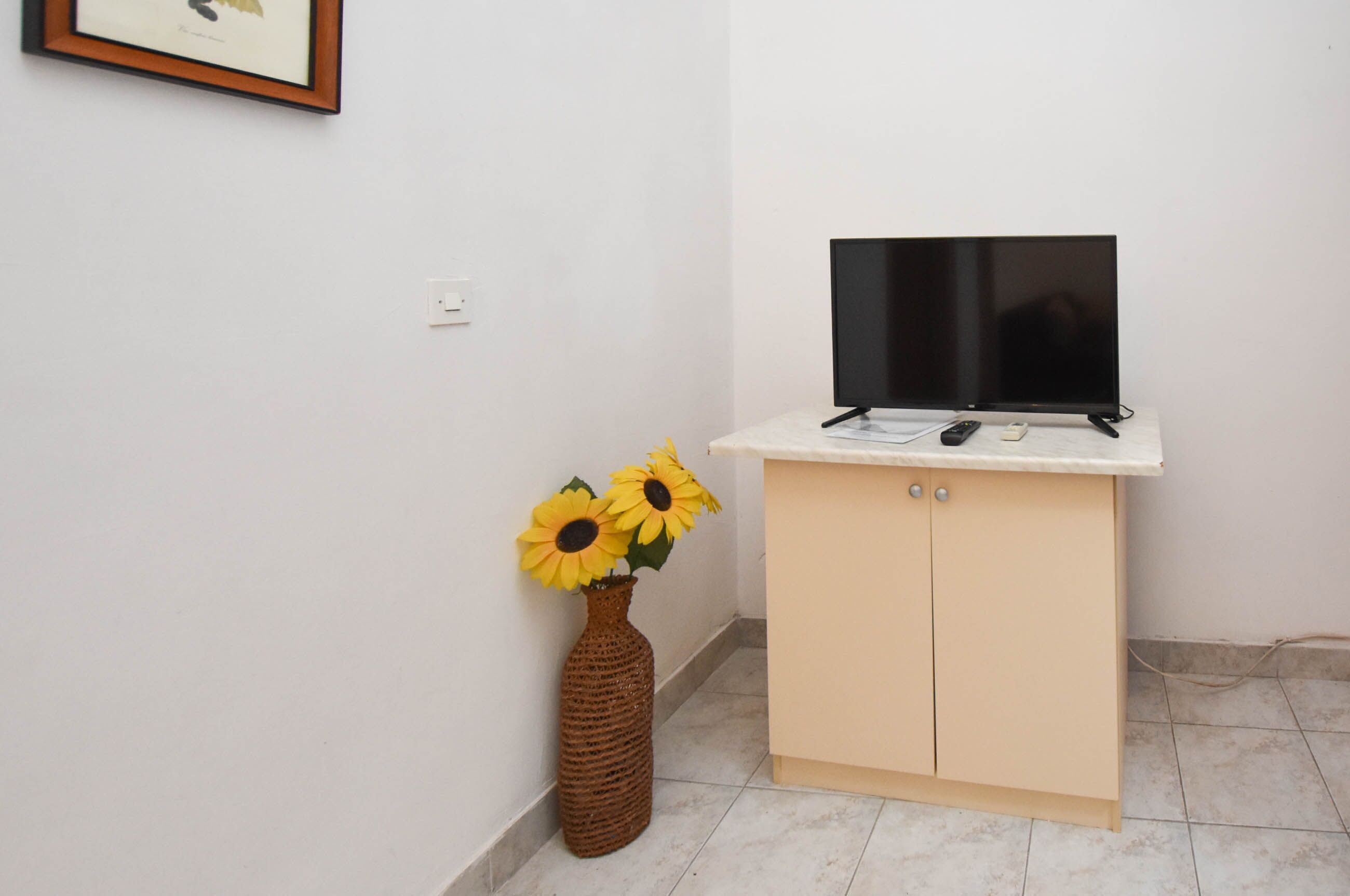 A room with a television on a cabinet, a vase with sunflowers, and a framed picture on the wall.