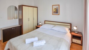 A neatly made bed with white linens and two folded towels, a wooden wardrobe, a bedside table with a lamp, and a framed picture on the wall. - Apartments Grapevines (Biograd)