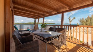 A wooden deck with a table and chairs, overlooking a beach and clear sky.