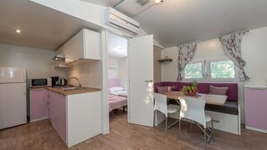 Cocina compacta con microondas, pileta y muebles bajos blancos. Un área de comedor con mesa y sillas está al lado de un sofá morado.