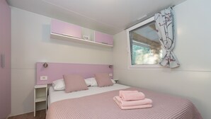 Un dormitorio con cama, ropa de cama rosa, una ventana con cortinas florales y cabecero rosa.