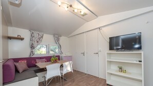 Una cocina moderna con una mesa de madera, sillas blancas, un sofá morado y un televisor sobre un soporte blanco.