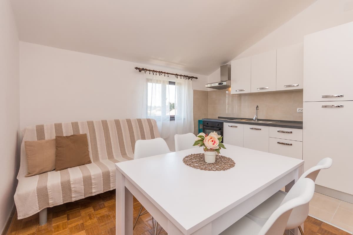 A modern kitchen with white cabinets, a dining table with chairs, and a striped sofa with cushions.