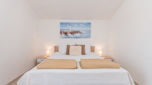 Ein Schlafzimmer mit einem Bett, zwei Nachttischen, einem Gemälde eines Leuchtturms und Holzboden.