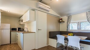 A compact kitchen with a microwave, coffee maker, and a small refrigerator. There is a dining area with a bench and two chairs. - Mobile Home Pecten 01 (Pakostane)