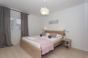 Ein ordentlich eingerichtetes Schlafzimmer mit einem hölzernen Bett, einem Nachttisch mit Lampe und Blick durch transparente Vorhänge.