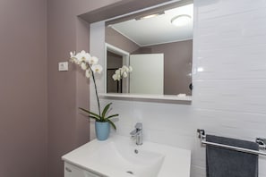 Ein Badezimmer mit einem weißen Waschbecken, einem Spiegel und einer Topf-Orchidee.