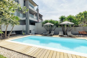 A swimming pool with lounge chairs and umbrellas, surrounded by a modern building with balconies. - Apartments Turritella (Biograd na Moru)