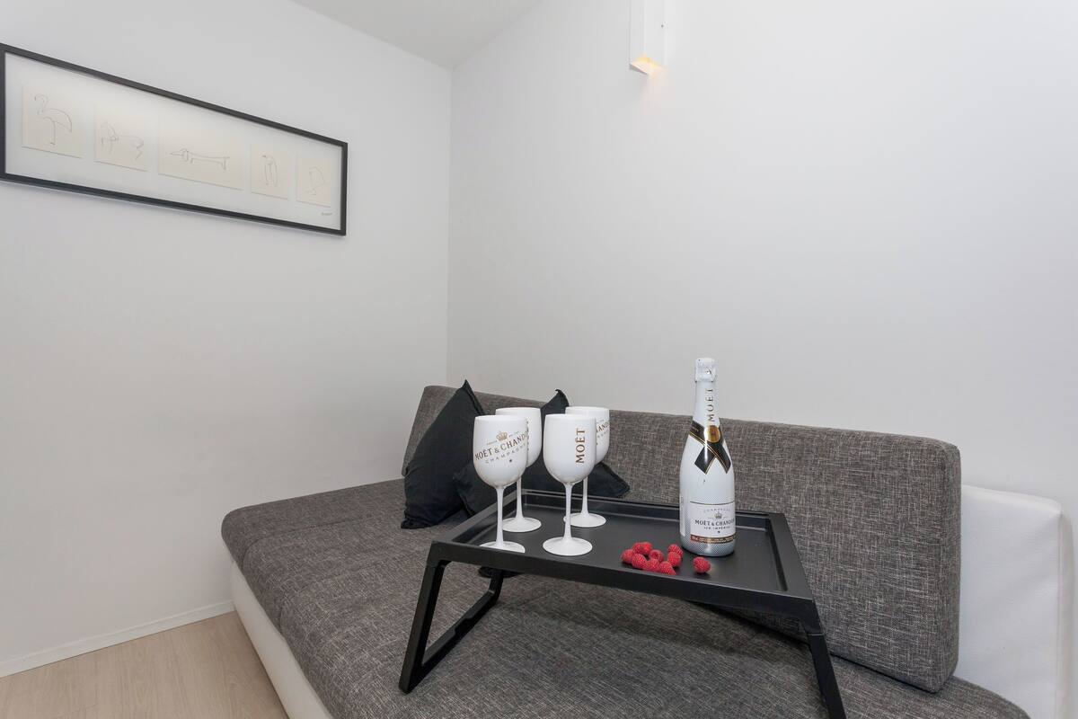 A modern living room with a grey sofa, a black coffee table, two wine glasses, a bottle of champagne, and a framed artwork on the wall.