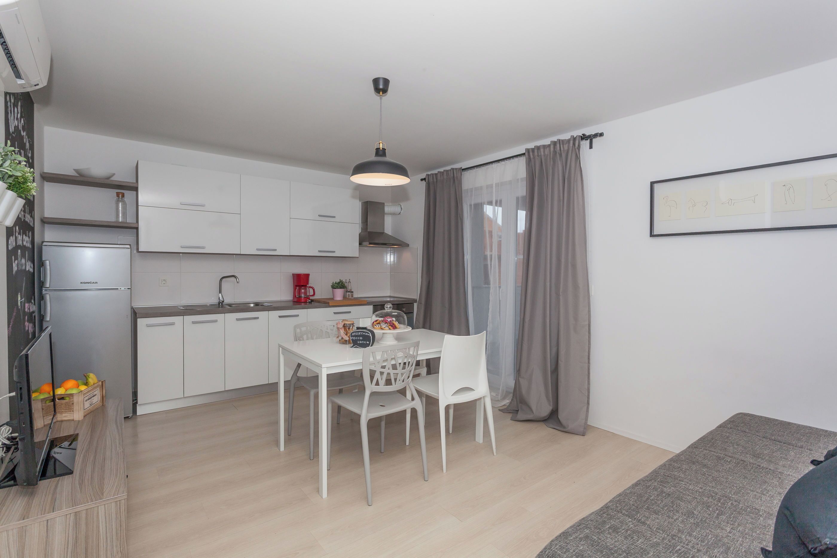 A modern kitchen with white cabinets, a dining table with chairs, and a grey pendant light.