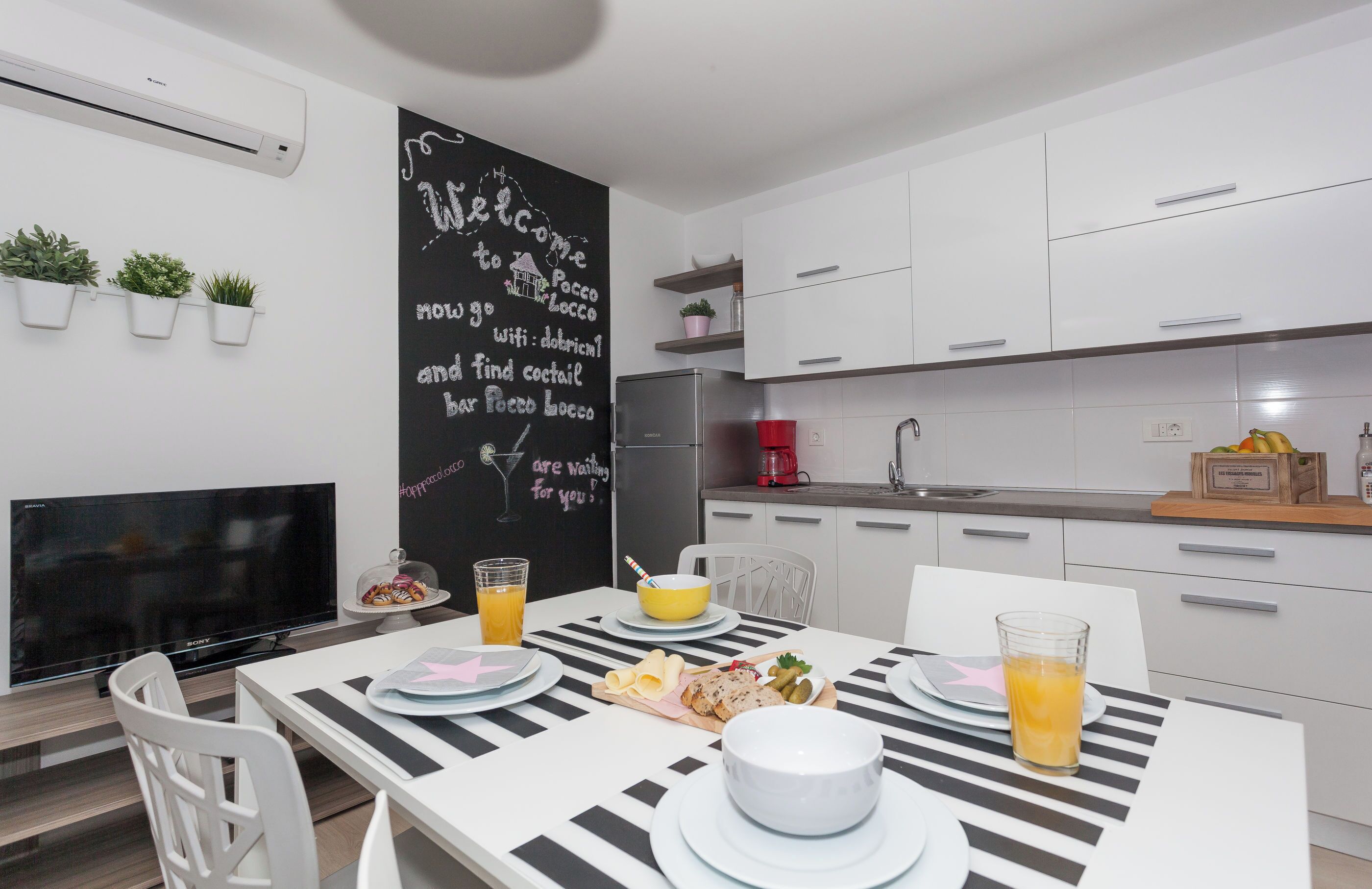A modern kitchen with white cabinets, a blackboard wall, and a dining area with a striped tablecloth.