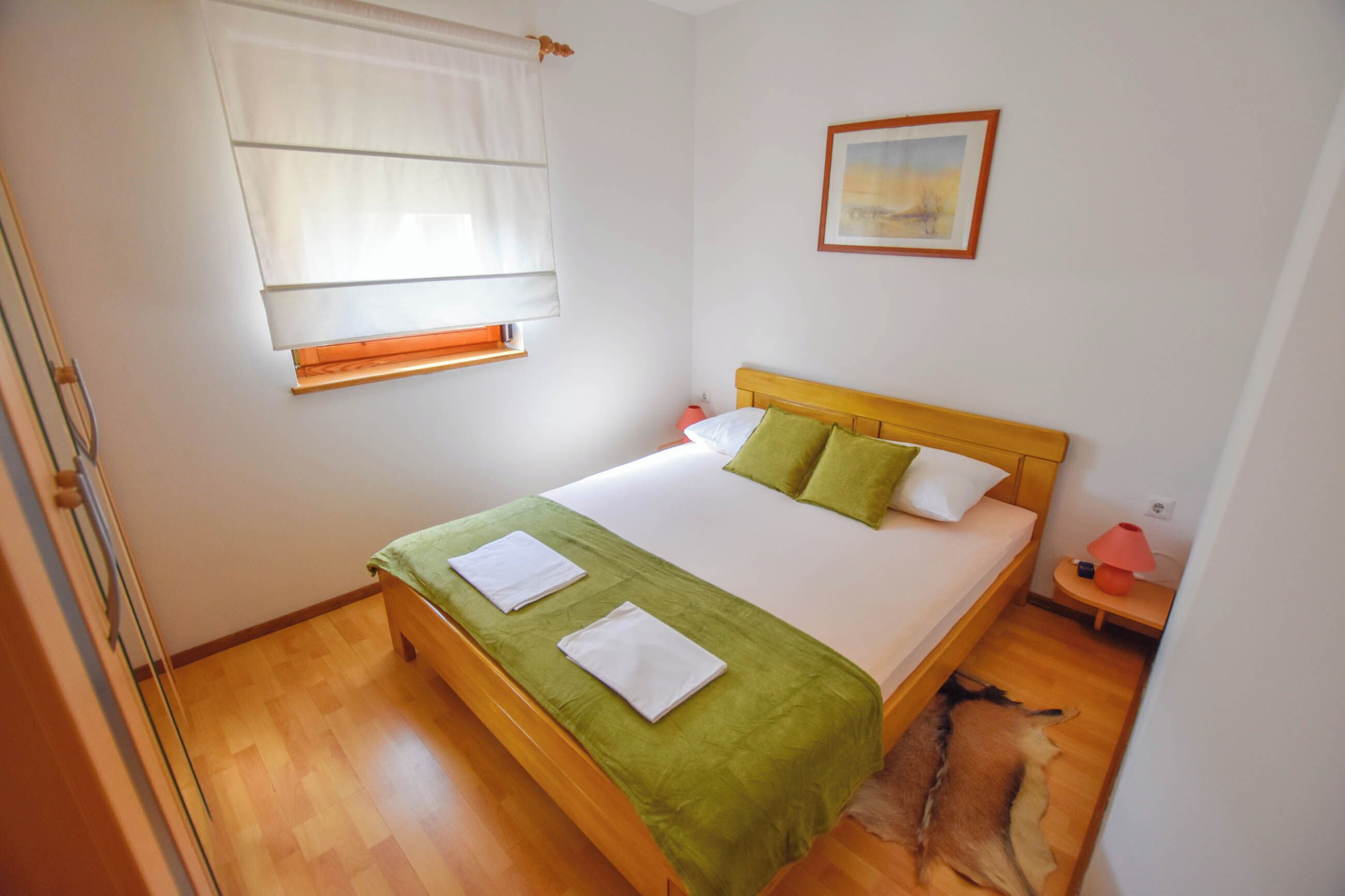 A neatly made bed with a green bedspread and pillows, a bedside table with a lamp, and a framed picture on the wall.