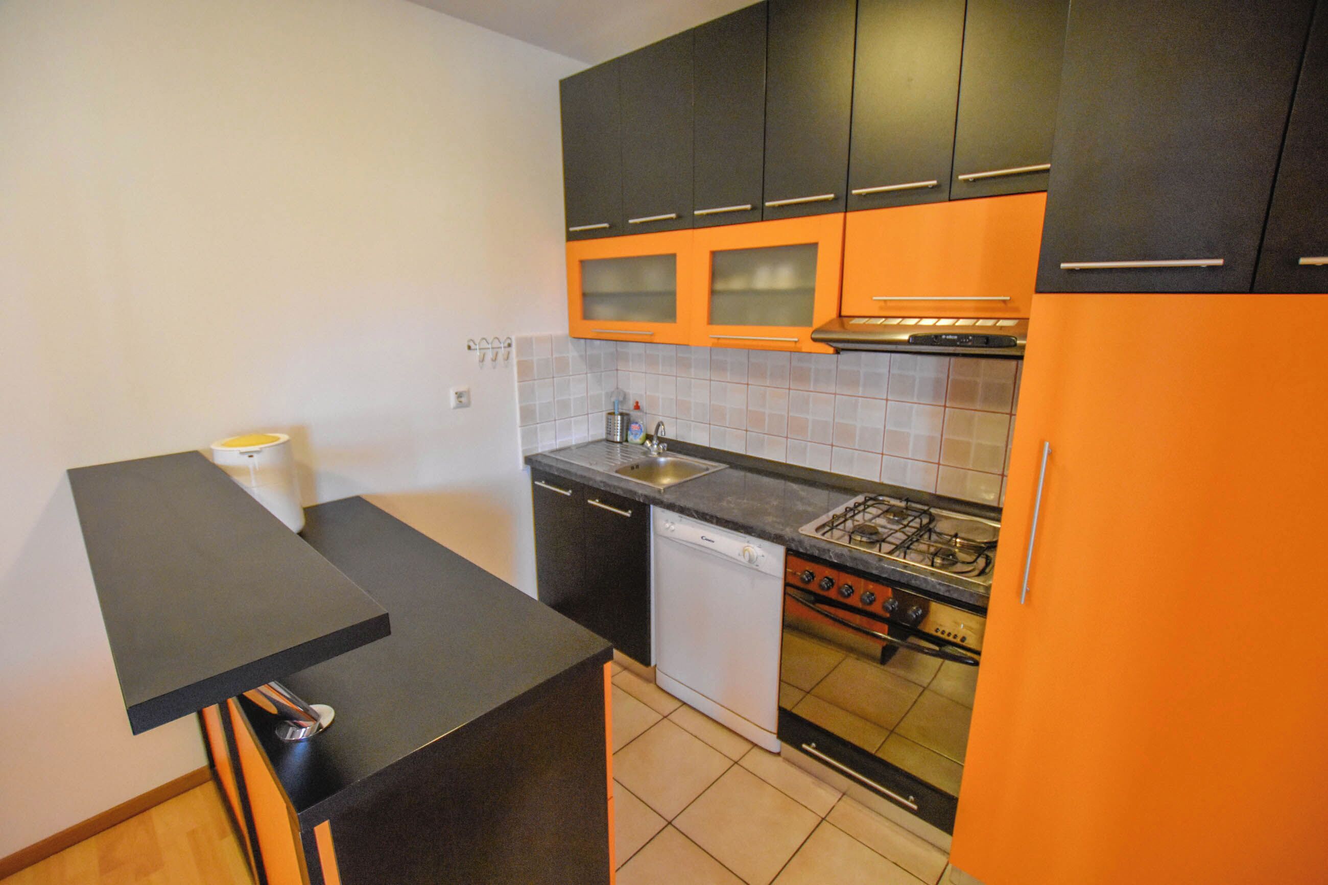 Una cocina compacta con gabinetes negros y anaranjados, un lavavajillas, una estufa y un fregadero.