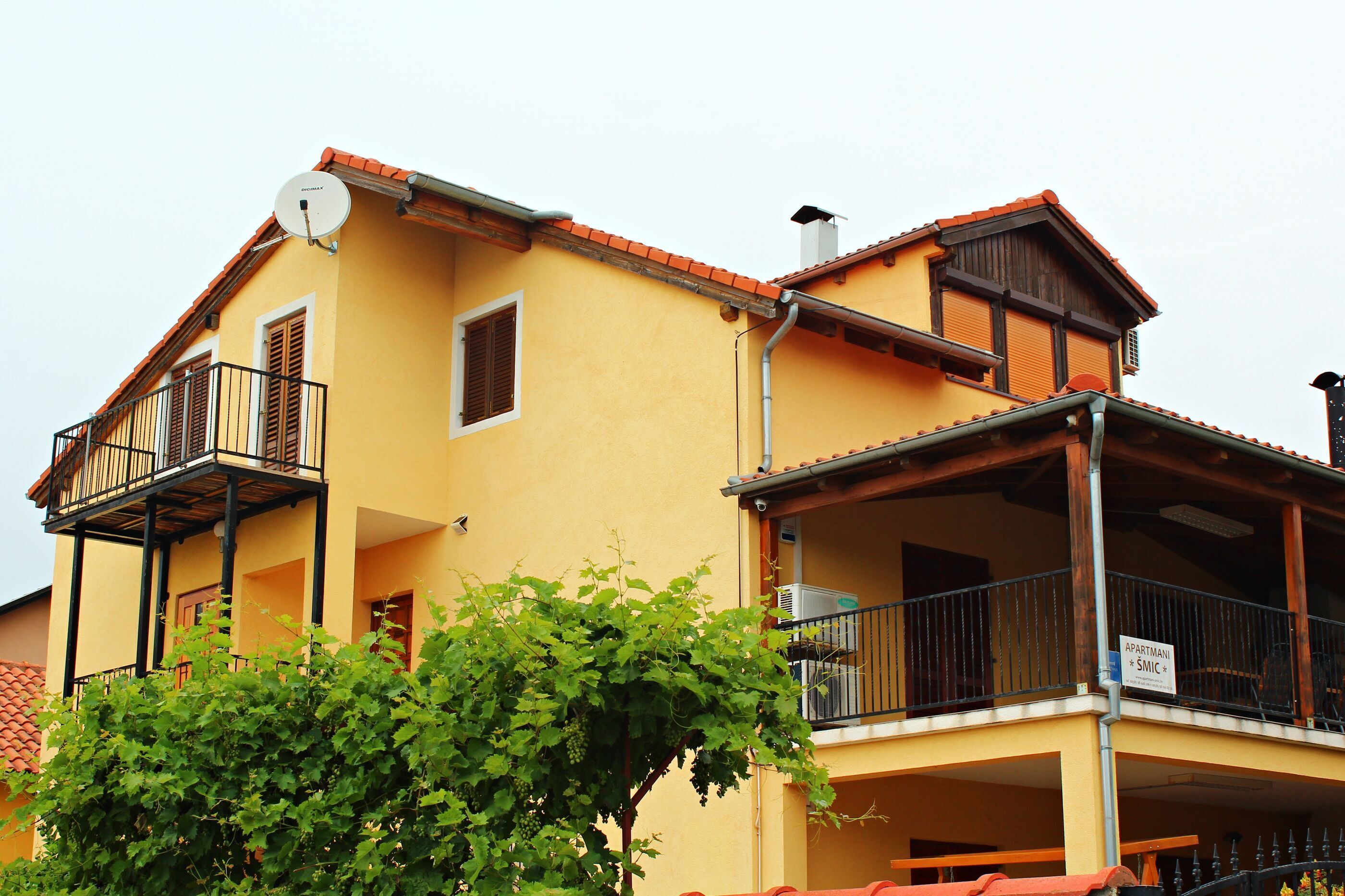 A yellow building with balconies, a satellite dish, and a sign indicating it is an apartment.