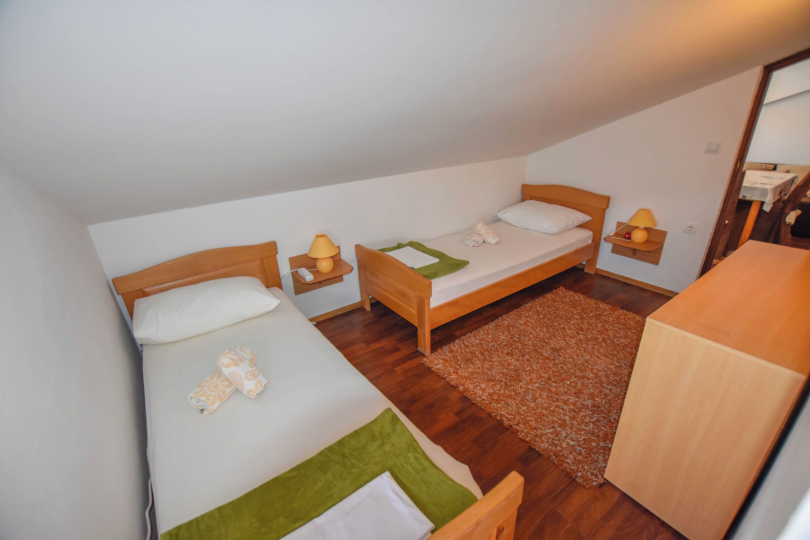 Ein kleines, gemütliches Zimmer mit zwei Einzelbetten, einem Holztisch und einem kleinen Tisch mit Lampe.