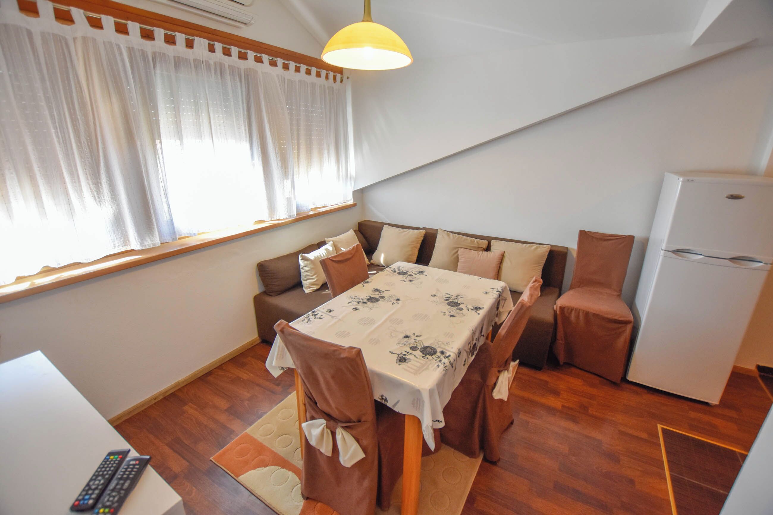 A compact living space with a dining table, chairs, a sofa, a refrigerator, and a window with curtains.