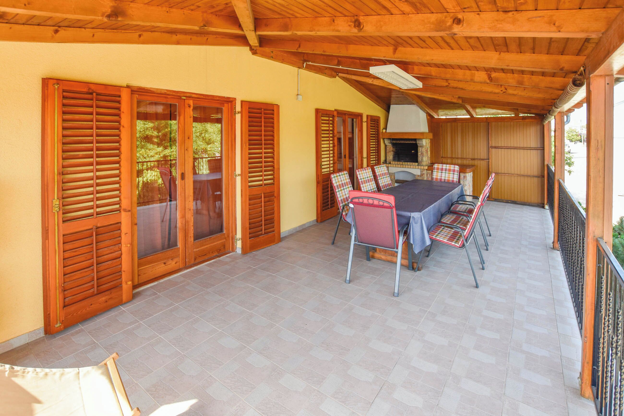 A covered patio with a dining table and chairs, wooden shutters, and a grill area.