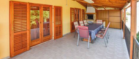 A covered patio with a dining table and chairs, wooden shutters, and a grill area.