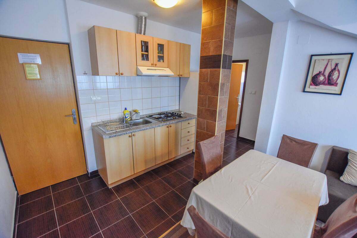 Une cuisine compacte avec des meubles en bois, une cuisinière à gaz et un évier. On y trouve également un coin repas avec une table et des chaises.