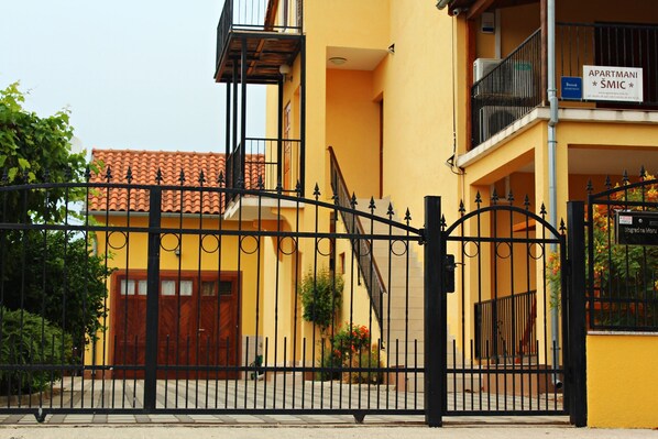 Un edificio amarillo con una verja de metal negra, una puerta de madera y un balcón con un cartel.