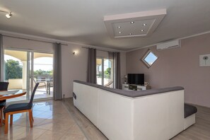 A modern living room with a central white sofa, a dining table with chairs, a TV, and a small window. - Apartments Svarog (Biograd)