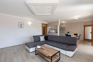 A modern living room with a grey sectional sofa, a wooden coffee table, and a kitchen in the background. - Apartments Svarog (Biograd)