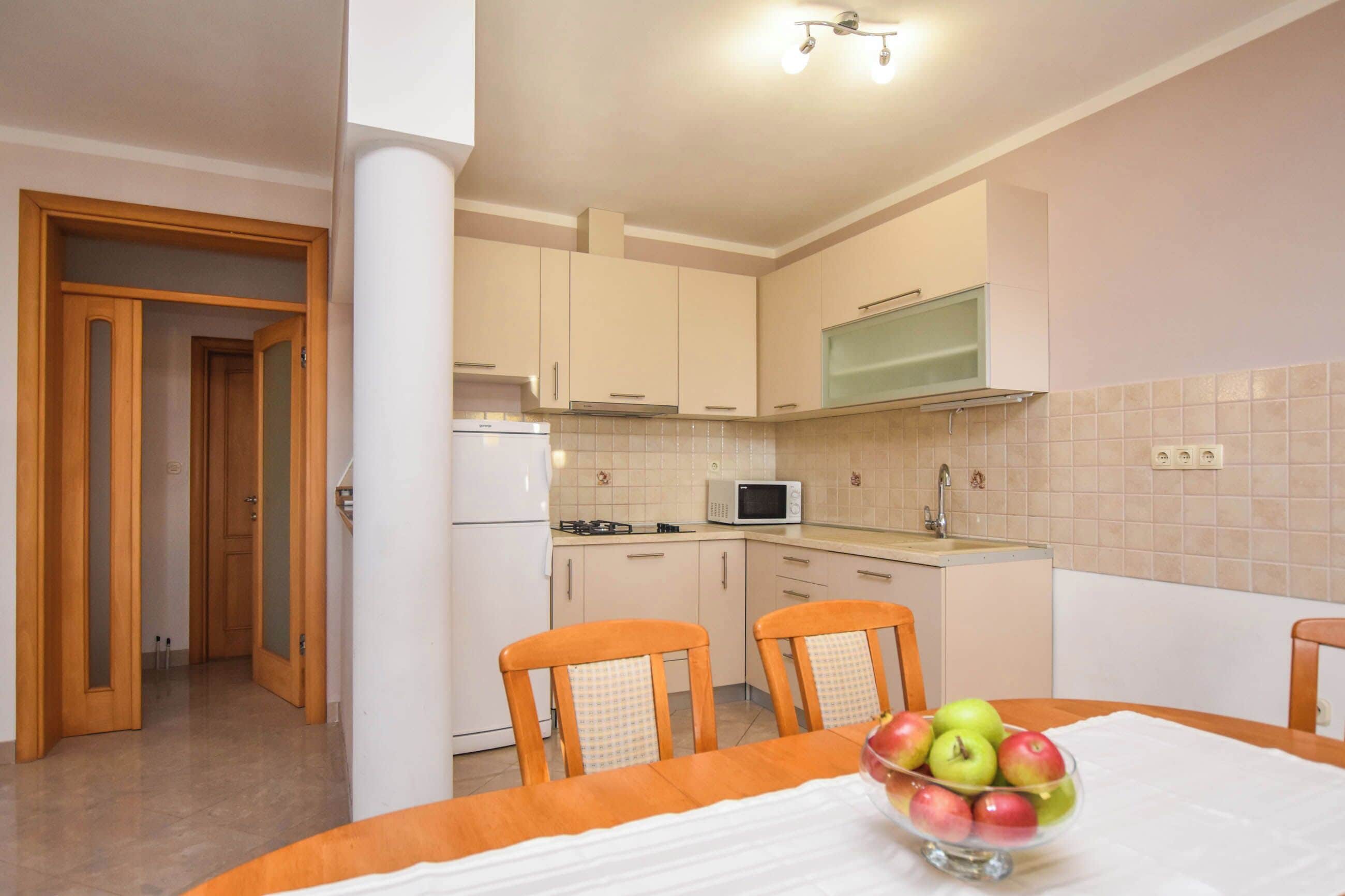 A compact kitchen with a microwave, stove, and sink. There is a dining table with chairs and a bowl of fruit.