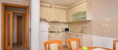 A compact kitchen with a microwave, stove, and sink. There is a dining table with chairs and a bowl of fruit.