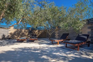Zona relax all'aperto con poltrone reclinabili e un tavolino, circondata da mura in pietra e ulivi.
