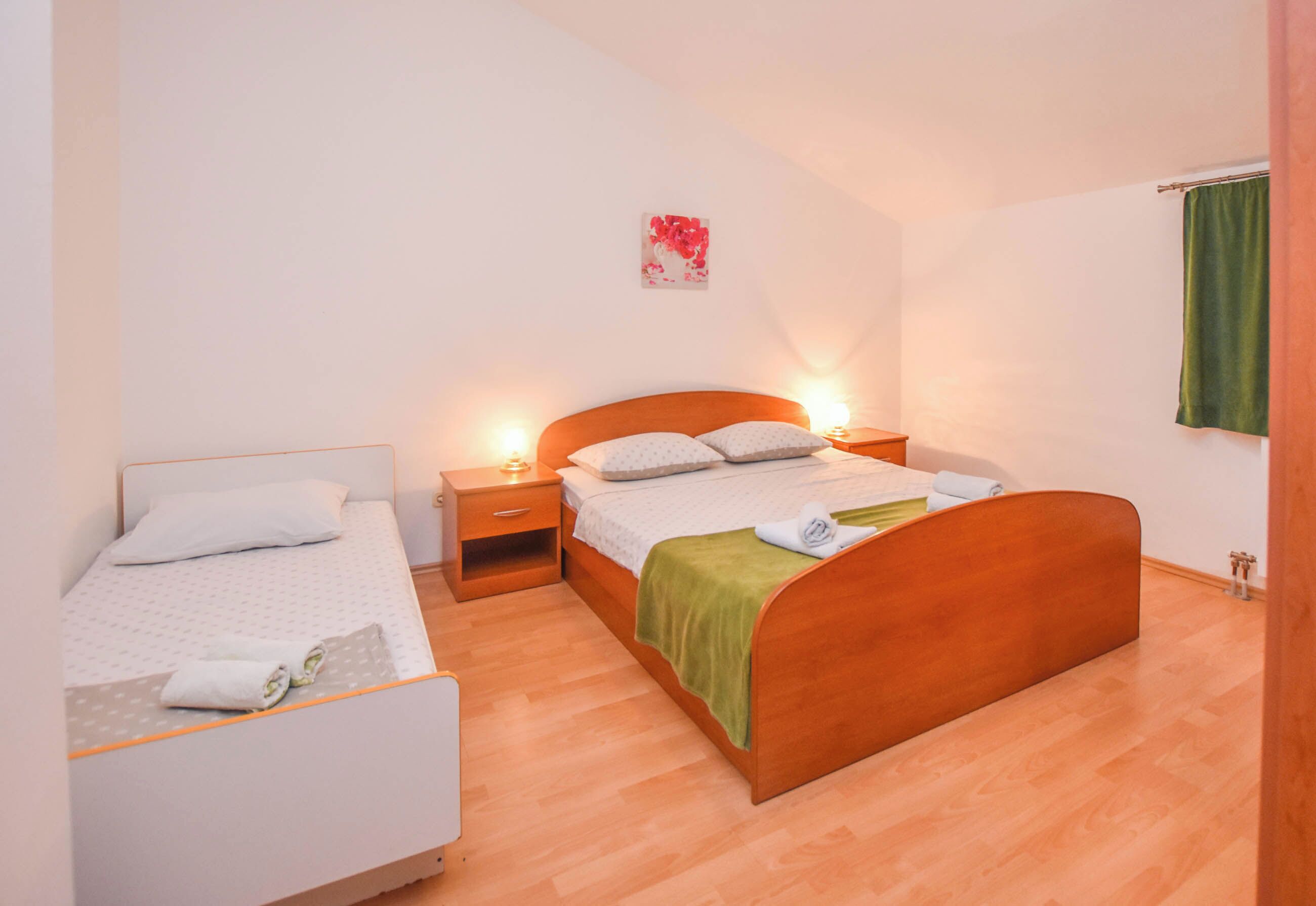 Ein Schlafzimmer mit zwei Einzelbetten, einem Holzkopfteil, Nachttischen mit Lampen und einem grünen Handtuch auf einem Bett.