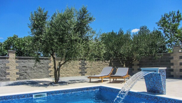A swimming pool with a water feature, surrounded by stone walls and trees. - Apartments Svarog (Biograd)