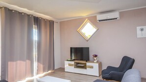 A modern living room with a flat-screen TV on a glass cabinet, grey sofas, a white coffee table, and a large window with curtains. - Apartments Svarog (Biograd)