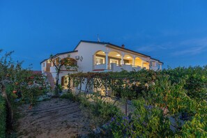 A two-story house with a covered porch and a garden in the foreground. - Apartments Svarog (Biograd)
