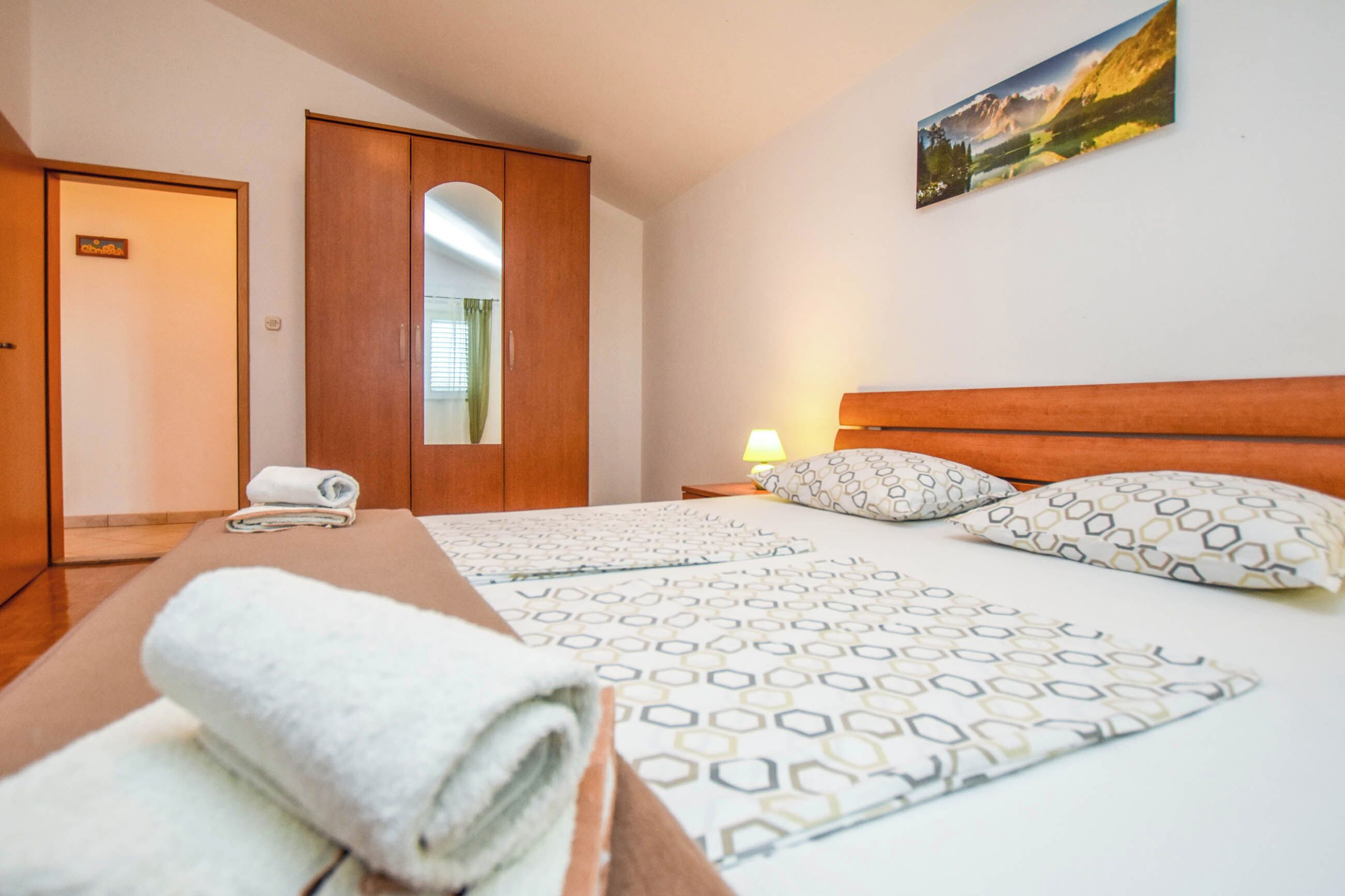 A hotel room with a bed, a wooden wardrobe, a mirror, and a painting on the wall.