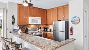 A kitchen with wooden cabinets, a microwave, a refrigerator, a stove, and a coffee maker. - 🌴 Perfect Island getaway | AC | Ocean View | AV #124🌴 (Kailua Kona)
