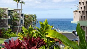 A hotel with a view of the ocean, surrounded by tropical plants and a parking area. - 🌴 Perfect Island getaway | AC | Ocean View | AV #124🌴 (Kailua Kona)
