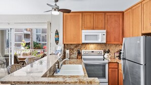A modern kitchen with wooden cabinets, a granite countertop, stainless steel appliances, and a dining area with outdoor views. - 🌴 Perfect Island getaway | AC | Ocean View | AV #124🌴 (Kailua Kona)