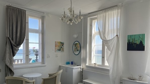 A bedroom with a bed, a desk, a chair, a small table, and a window with curtains.