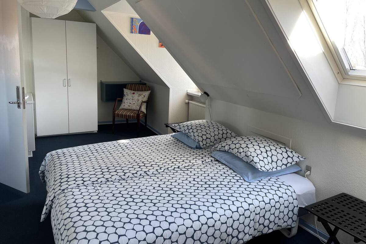 Quarto com cama, cadeira, escrivaninha e janela.